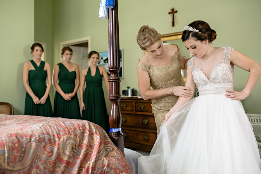 A bride putting on her wedding dress while her mother helps.